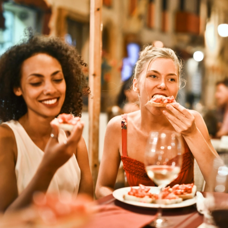 Two women sitting in a restaurant eating pizza with wine on the table